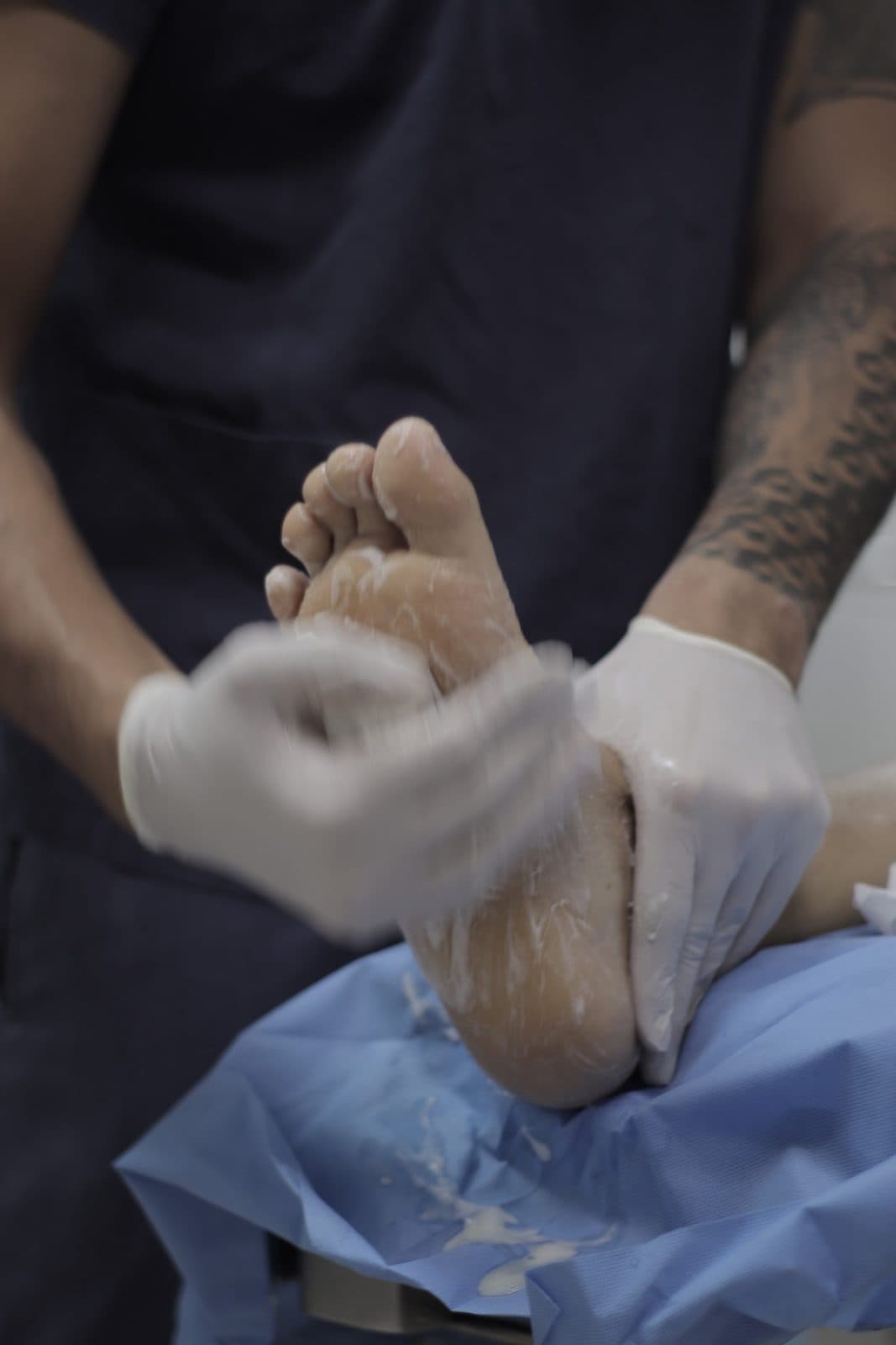Mãos com luvas cirúrgicas posicionando o pé do paciente no centro cirúrgico